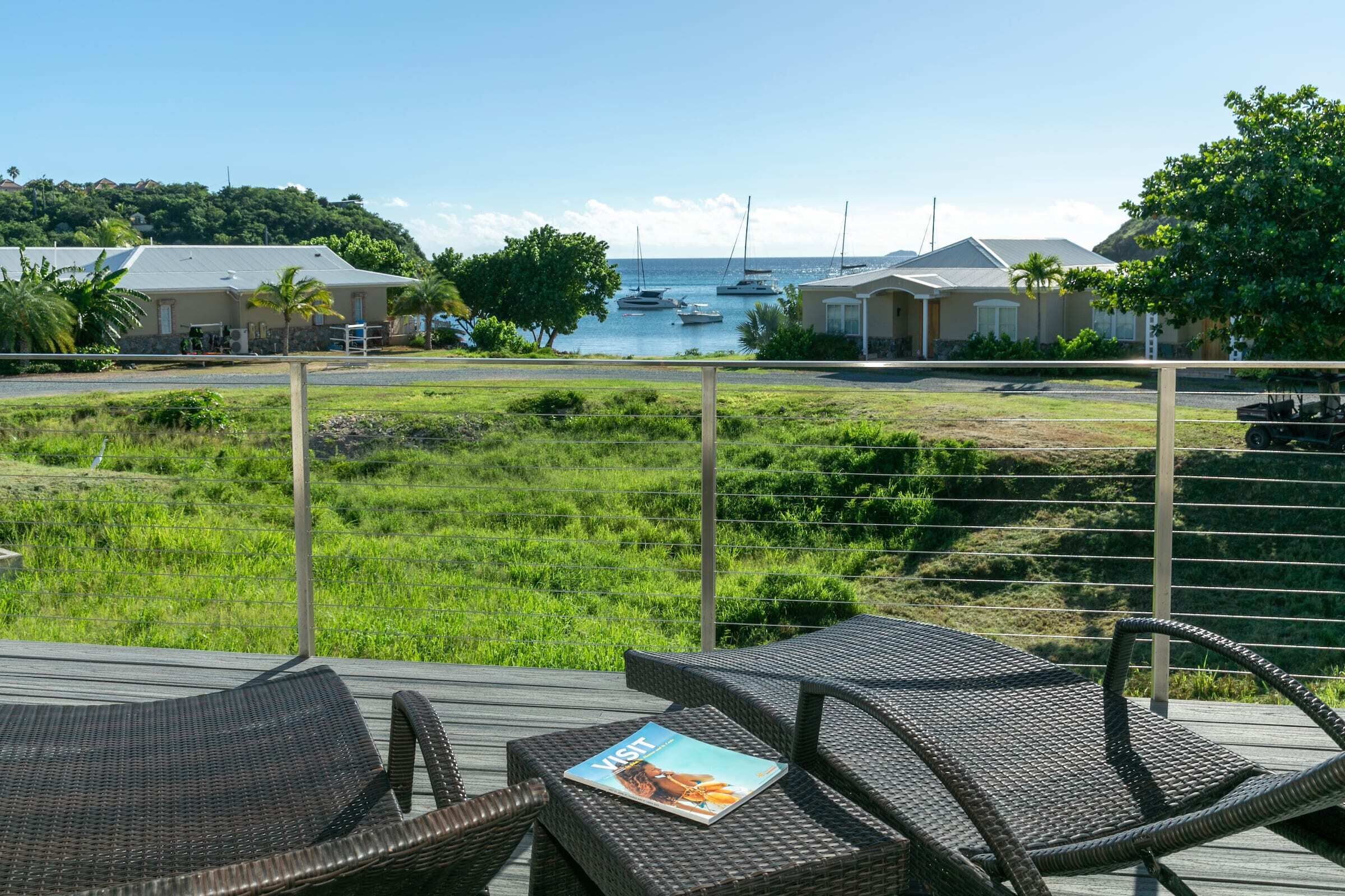 A deck with wicker chairs and a magazine, overlooking a marina with boats and houses.