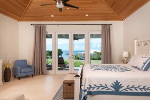 A bedroom with a bed, a chair, a lamp, and a view of the outdoors. - Pirates Villa- Beach view with kayaks for Groups (Cruz Bay)