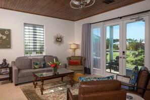 Ein Wohnzimmer mit Sofa, Sessel, Couchtisch und Blick durch eine Glasschiebetür.