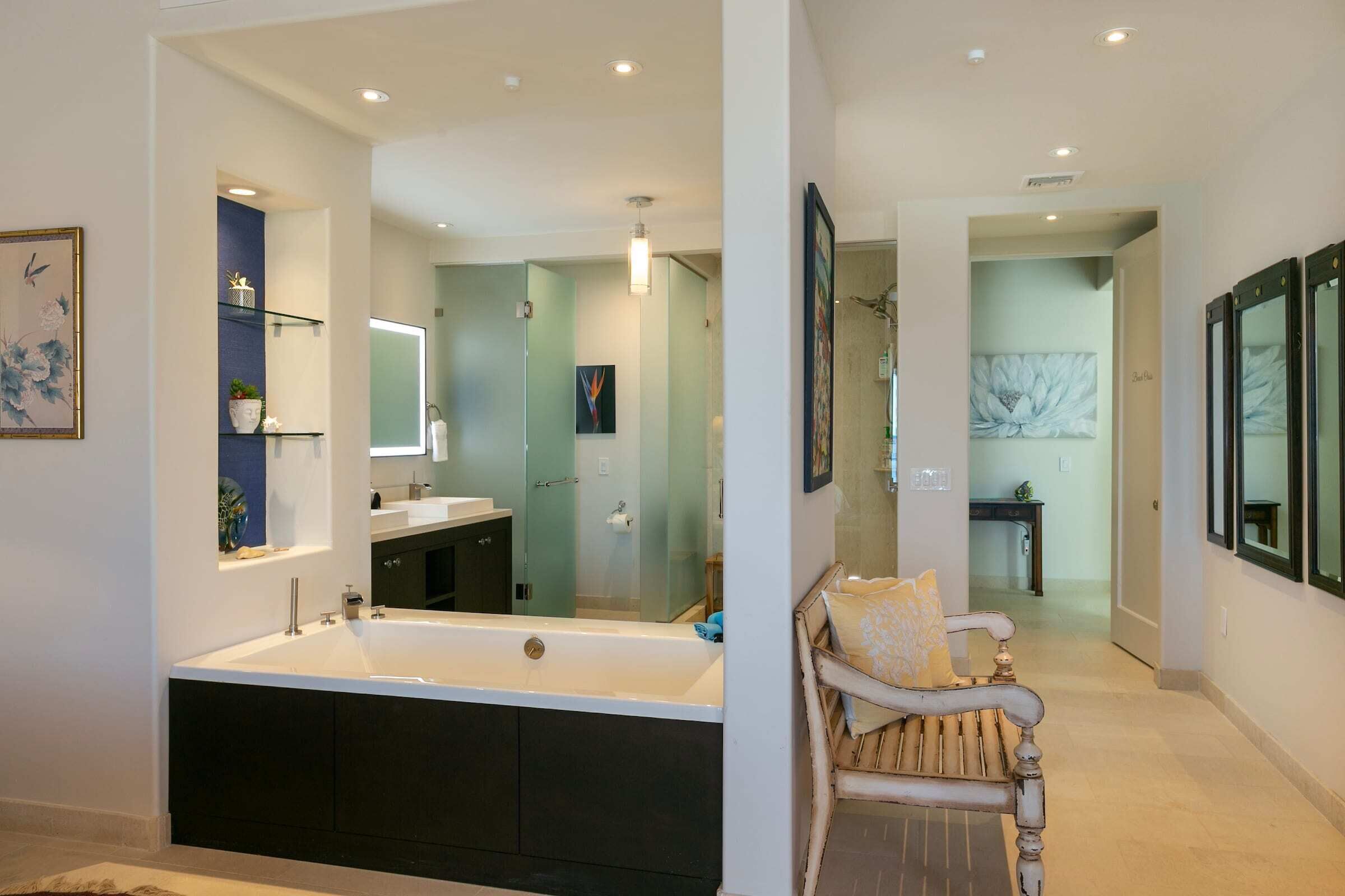 Ein modernes Badezimmer mit einer großzügigen Badewanne, einem Waschtisch und einer Dusche. Im Flur befindet sich eine Bank mit Kissen.