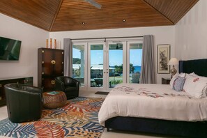 Ein Schlafzimmer mit einem großen Bett, Holzboden, einem Fernseher, einem Kleiderschrank und Blick ins Freie.