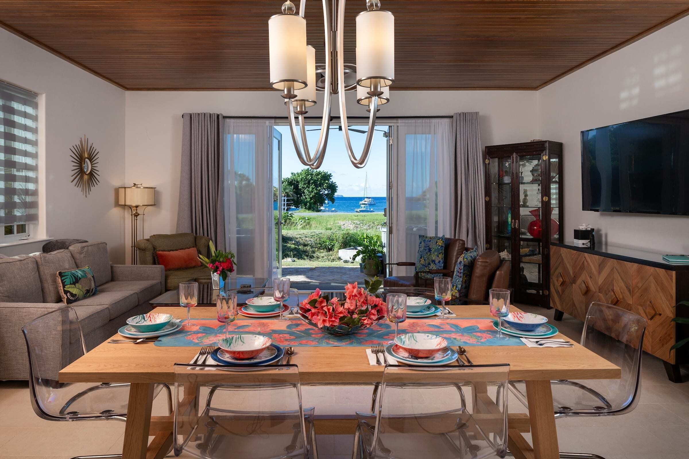 A modern dining room with a large table, clear glass chairs, and a view of the sea.