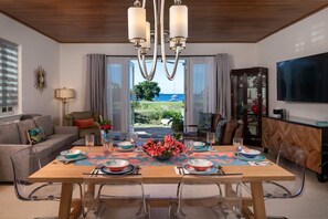 Ein stilvolles Esszimmer mit großem Tisch, transparenten Stühlen und Blick aufs Meer.