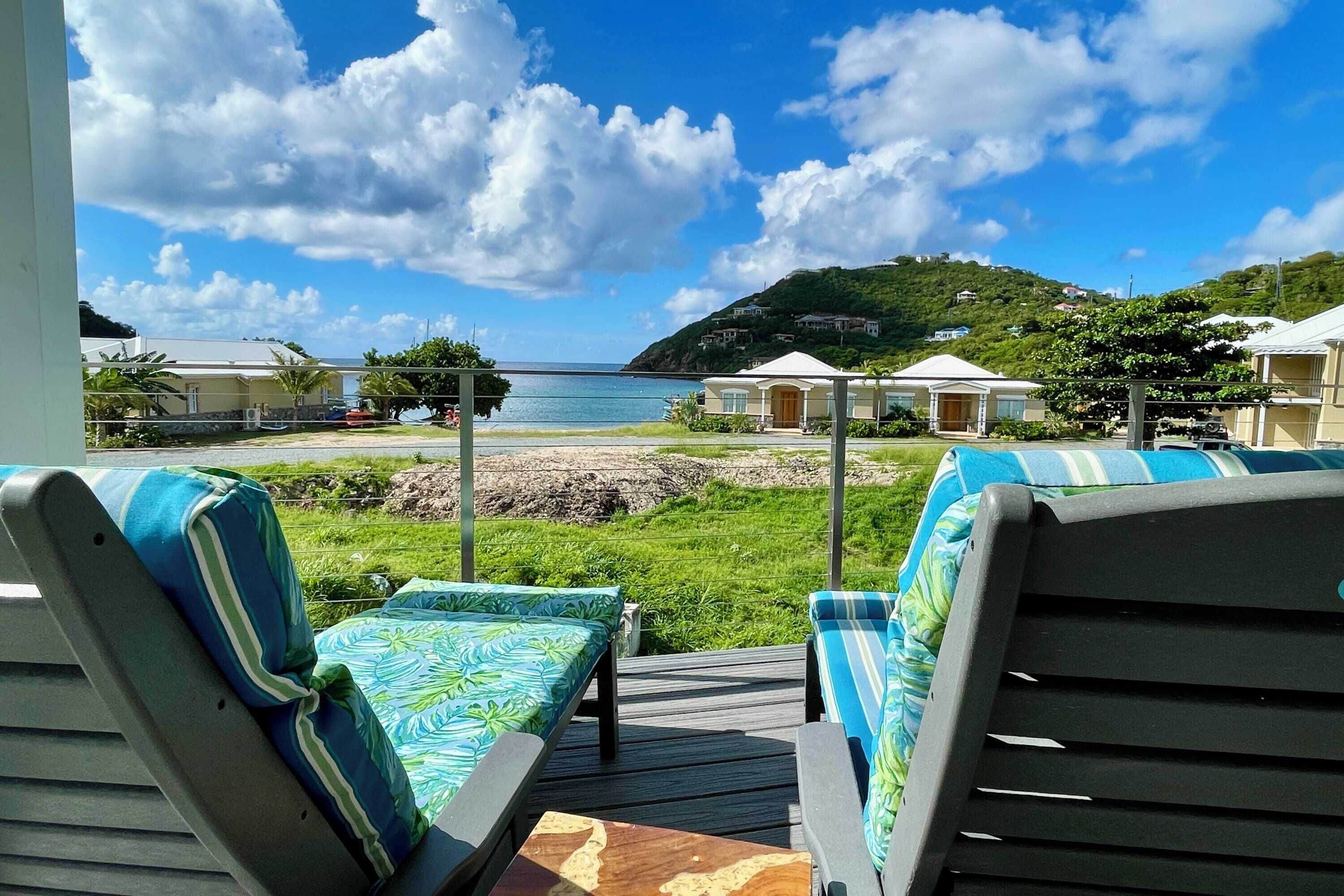 Une terrasse dotée de deux chaises longues, d’une petite table et offrant une vue sur la mer et les collines en arrière-plan.