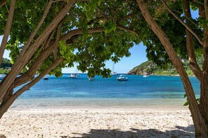 Ein Strand mit klarem türkisblauem Wasser, Booten und einer von Bäumen gesäumten Uferlinie.