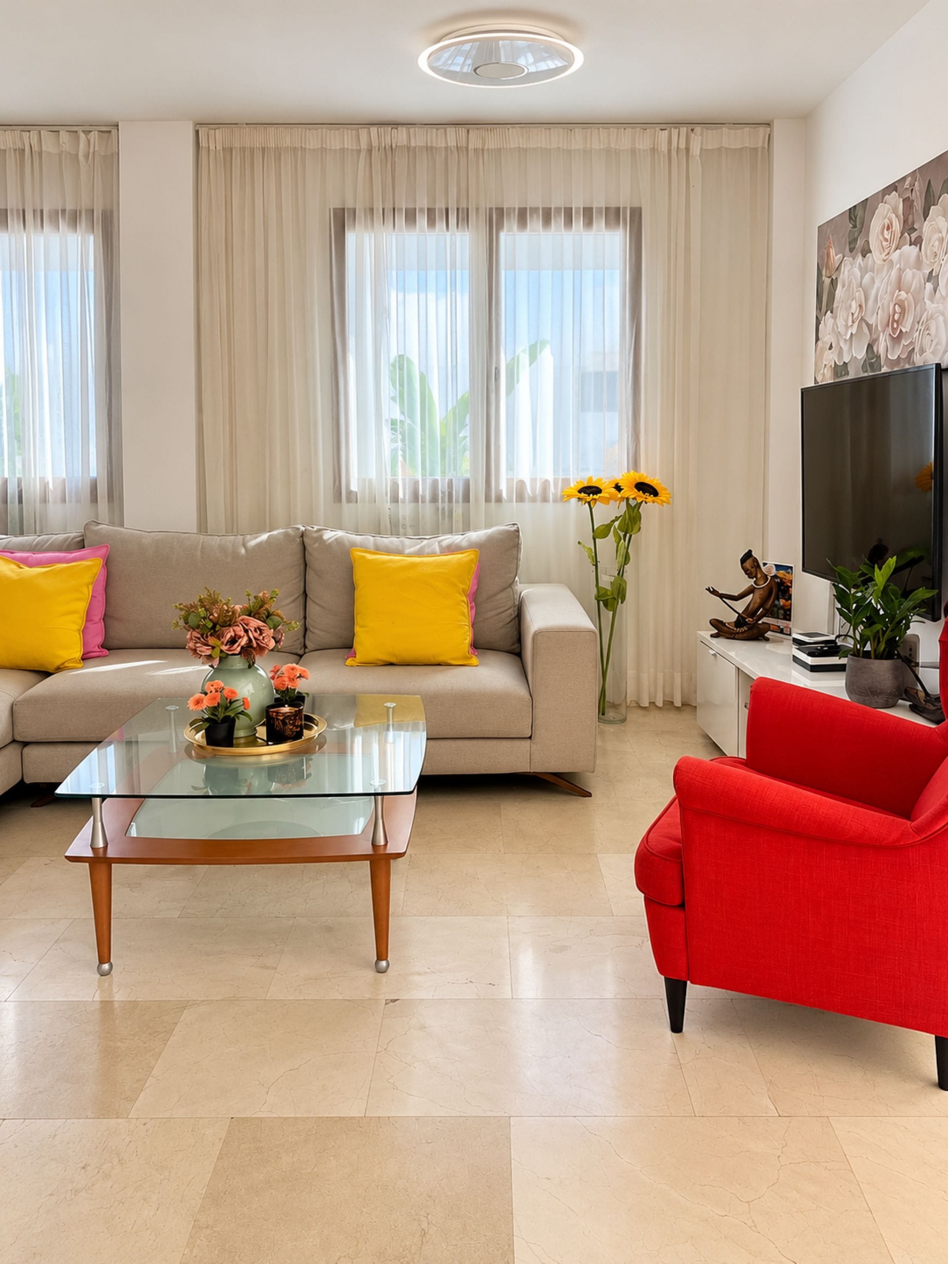 Un salon avec un canapé, un fauteuil rouge, une table basse en verre et un téléviseur à écran plat.
