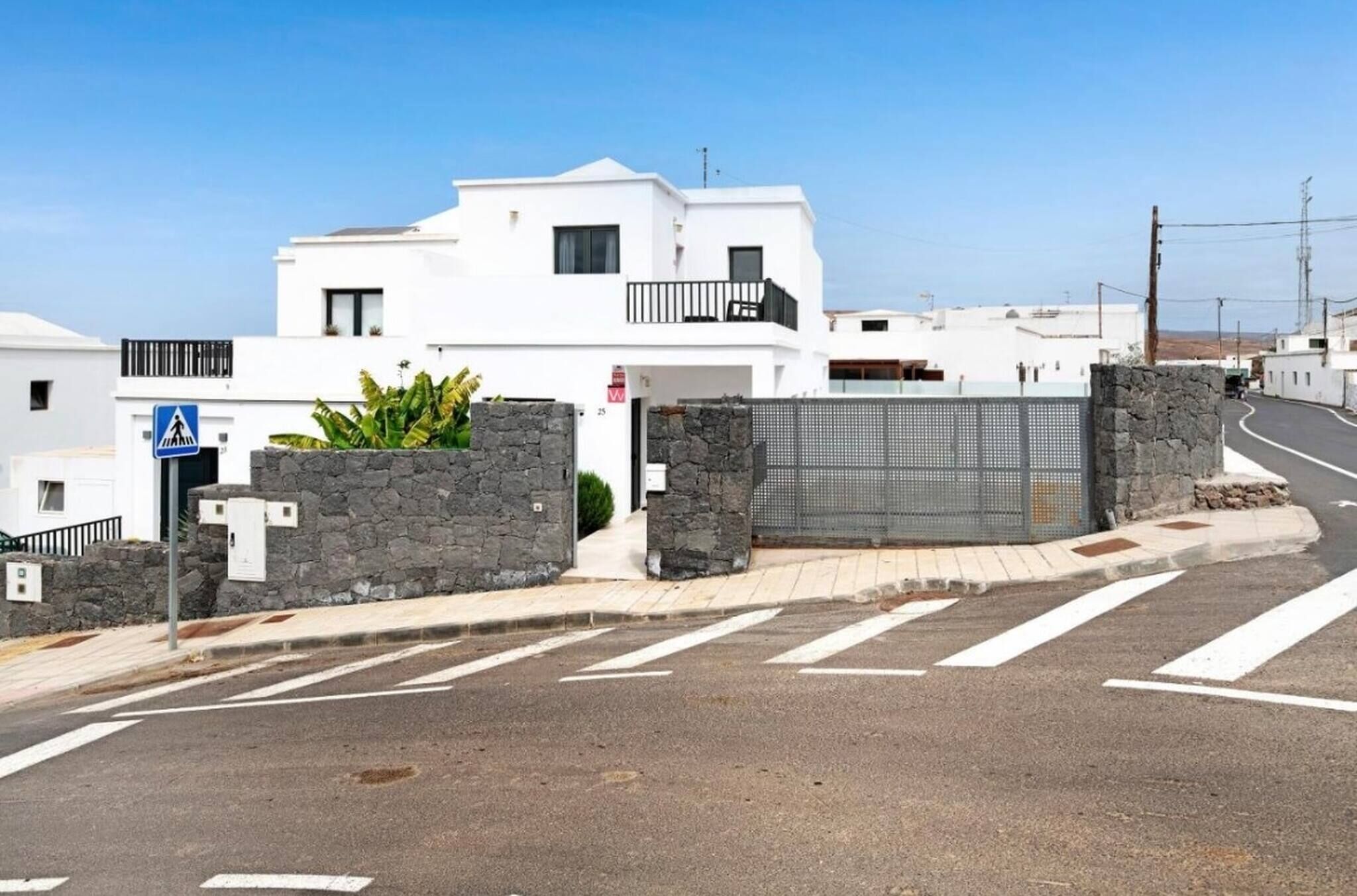Un bâtiment moderne de couleur blanche, doté d’une entrée sécurisée par un portail, d’un passage piéton et surplombant un ciel dégagé.