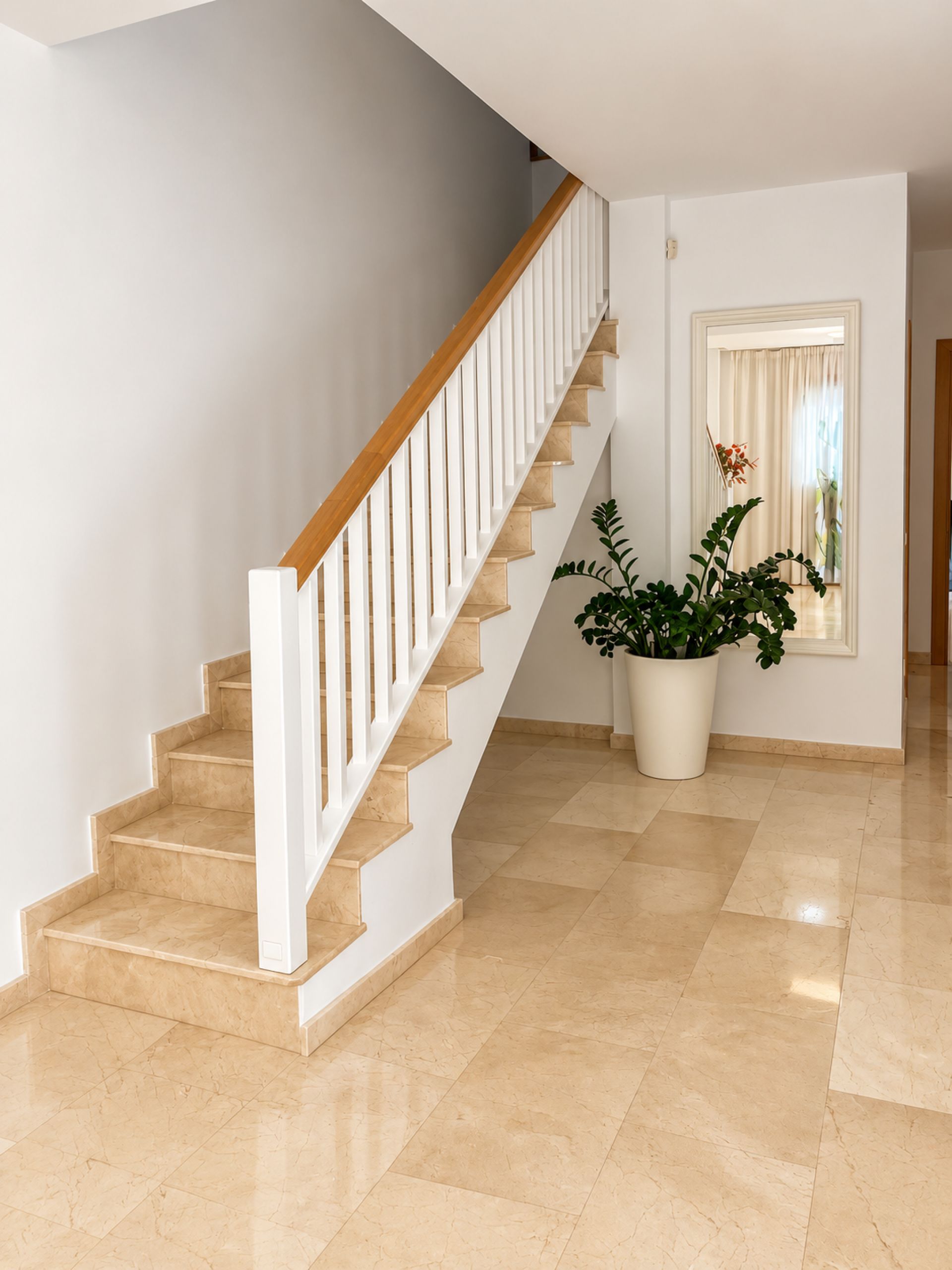 Eine Treppe mit weißen Geländern und beigen Stufen, die zu einer Zwischenebene führt.