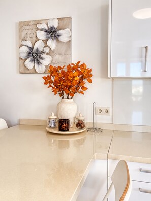 Eine Küche mit einer Marmorarbeitsplatte, einer Vase mit orangefarbenen Blättern und einem Gemälde an der Wand.