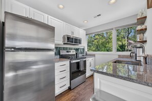 A modern kitchen with stainless steel appliances, white cabinetry, and a large window providing a view of trees. - Golf Course Oasis·Hot Tub·Family Fun·Club Pool (Galena)