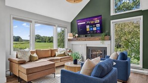 Een moderne woonkamer met een grote televisie, comfortabele zithoek en een open haard.