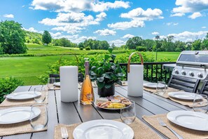 An outdoor dining area with a table set for four, a grill, and a scenic view of a golf course. - Golf Course Oasis·Hot Tub·Family Fun·Club Pool (Galena)