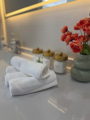 Ein Badezimmer mit weißem Waschtisch, einer Vase mit rosa Blumen und ordentlich gefalteten weißen Handtüchern.