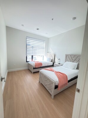 Ein Schlafzimmer mit zwei Betten, einem Fenster mit Jalousien und einem hellen Holzboden.