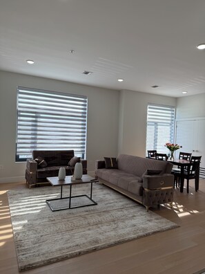 Ein modernes Wohnzimmer mit einer Eckcouch, einem Couchtisch und einem Essbereich mit Tisch und Stühlen.