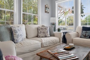 A living room with a beige sofa, patterned pillows, a coffee table with magazines, and a window with blinds. - Beach Breeze Bungalow (Fort Myers)