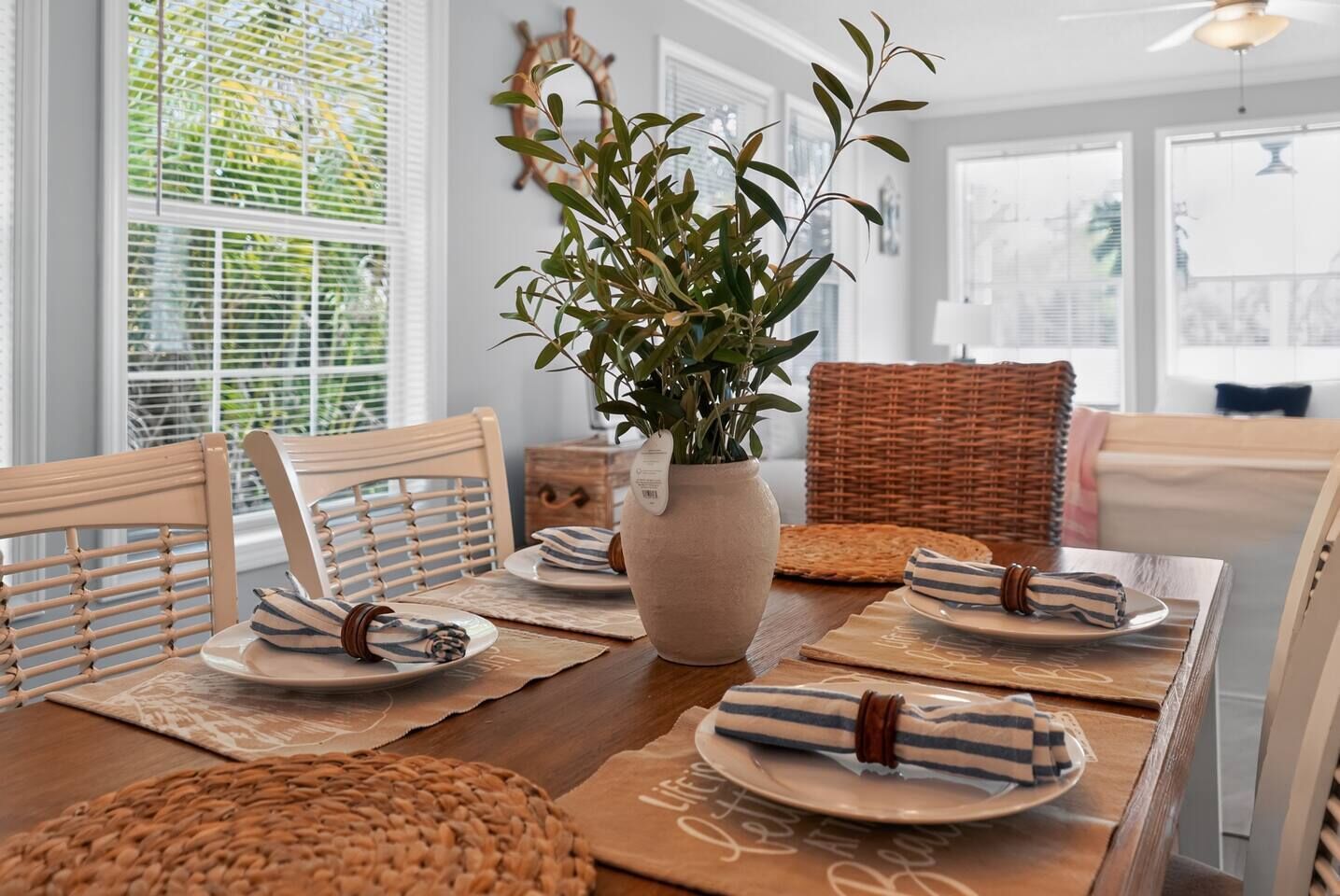 Une table à manger dressée avec des assiettes, des serviettes et un vase rempli de verdure.