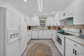 A modern kitchen with white cabinetry, a built-in dishwasher, a stove, and a sink. - Beach Breeze Bungalow (Fort Myers)