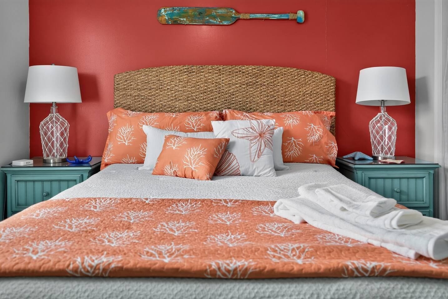 A bed with a woven headboard, multiple pillows with a leaf pattern, and a blanket with a similar design. There are two bedside tables with lamps and decorative items.