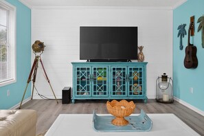 A living room with a teal cabinet, a television, a tripod, and a wicker bowl on a tray. - Beach Breeze Bungalow (Fort Myers)