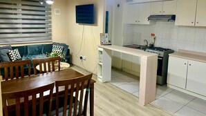 Una cocina compacta con comedor, un televisor montado en la pared y un ventanal con persianas.
