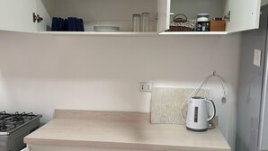 Cocina con armarios blancos, estufa a gas, hervidor y diversos utensilios de cocina.