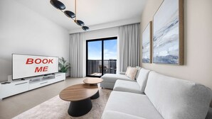 A modern living room with a flat-screen TV, a sofa, a coffee table, and a balcony with a city view. - Free Housekeeping Visits During Your Stay - Stayshort - Chic 1-bed for 4 in Prime Dubai Hills Location (Dubai)
