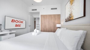 A hotel room with a bed, a desk with a chair, a TV, and a door leading to a bathroom. - Free Housekeeping Visits During Your Stay - Stayshort - Chic 1-bed for 4 in Prime Dubai Hills Location (Dubai)