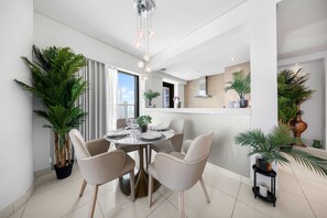 A modern dining area with a round table, white chairs, and potted plants. - Free Housekeeping Visits During Your Stay - Stayshort - Modern 2BR in Prime Business Bay 4 Guests (Dubai)