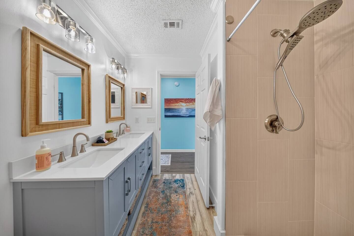 A modern bathroom with a double sink vanity, a shower with a handheld showerhead, and a blue accent wall.