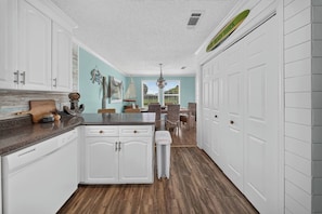 A kitchen with white cabinets, a granite countertop, and a dining area with a table and chairs. - 3BR/2BA Beach House-Tiki Bar! King ensuite w/ deck (Fort Myers)