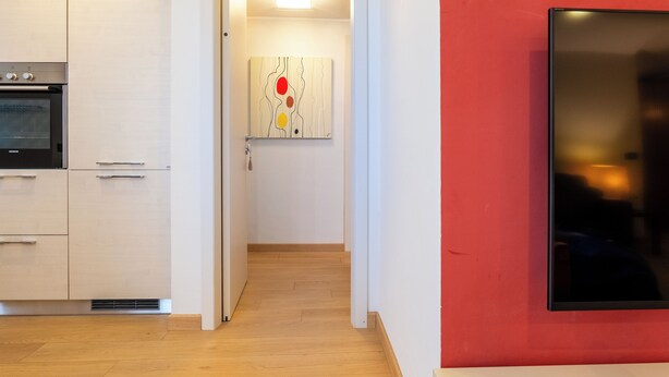 Eine moderne Küche mit Einbaugeräten, ein Flur, der in einen Wohnbereich führt, und eine rote Akzentwand.