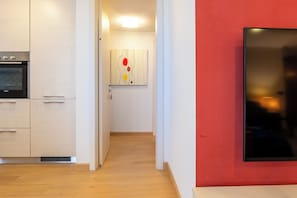 A modern kitchen with built-in appliances, a hallway leading to a living area, and a red accent wall.