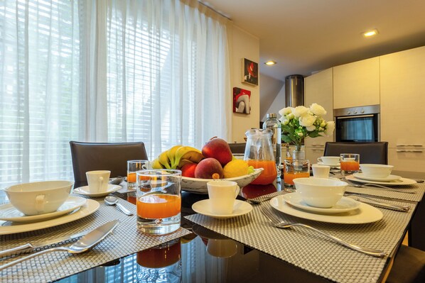A breakfast setting with a table set for two, including plates, cups, cutlery, and a fruit bowl.