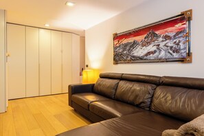 Una habitación con un sofá de cuero marrón, un cuadro de un paisaje montañoso, suelo de madera y un armario blanco.