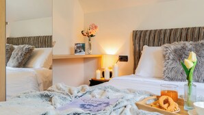 Ein Hotelzimmer mit zwei Betten, einem Nachttisch mit Blumenvase, einer Ablage mit Snacks und einem Glas Orangensaft.