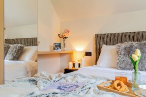 A hotel room with two beds, a nightstand with a vase of flowers, a tray with snacks, and a glass of orange juice. - The Ridge | Family Apartment with Matterhorn View (Breuil-Cervinia)