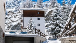 A mountain cabin with a wooden upper floor and a white lower floor, surrounded by snow-covered trees and mountains. - Cretaz Nest - Central Studio near Ski Lifts (Breuil-Cervinia)