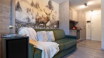 Een woonkamer met een groene bank, een schilderij van een hert en een keuken met houten kasten.
