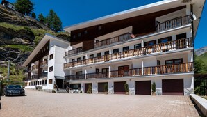 A multi-story hotel with balconies, a paved driveway, and a car parked in front. - Cretaz Nest - Central Studio near Ski Lifts (Breuil-Cervinia)