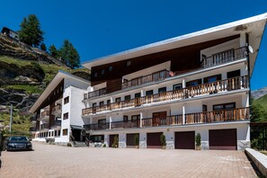 A multi-story hotel with balconies, a paved driveway, and a car parked in front. - Cretaz Nest - Central Studio near Ski Lifts (Breuil-Cervinia)