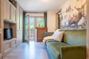 A room with a green sofa, wooden cabinets, a television, and a painting of deer. - Cretaz Nest - Central Studio near Ski Lifts (Breuil-Cervinia)