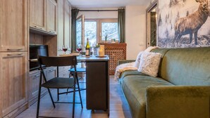 A cozy living room with a sofa and a television, a dining area with a table and chairs, and a kitchen with cabinets and a window. - Cretaz Nest - Central Studio near Ski Lifts (Breuil-Cervinia)