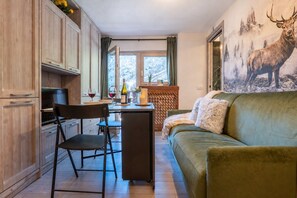 A cozy living room with a sofa and a television, a dining area with a table and chairs, and a kitchen with cabinets and a window. - Cretaz Nest - Central Studio near Ski Lifts (Breuil-Cervinia)