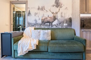 A green sofa with a blanket and pillows, a mirror, and a wall with a deer and forest mural. - Cretaz Nest - Central Studio near Ski Lifts (Breuil-Cervinia)