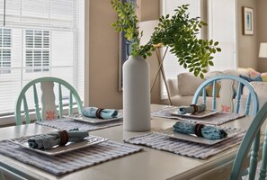 A dining table set with placemats, folded napkins, and a vase with greenery. - 3BR/2BA Beach House! Sleeps 9 w/ 2 Living rms-W/D! (Fort Myers)