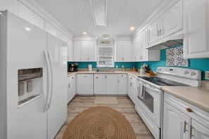 A kitchen with white cabinets, a built-in oven, a stove, and a coffee maker. - 3BR/2BA Beach House! Sleeps 9 w/ 2 Living rms-W/D! (Fort Myers)