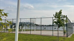 Een gazon met een witte paal, een hek en een basketbalveld.