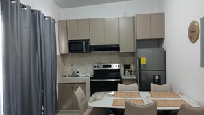 Een compacte keuken met een eethoek, inclusief een magnetron, fornuis, koelkast en een eettafel met stoelen.