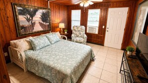 A bedroom with a bed, a chair, a ceiling fan, a painting, and a door. - Cozy Florida Stay in Bradenton (Bradenton)